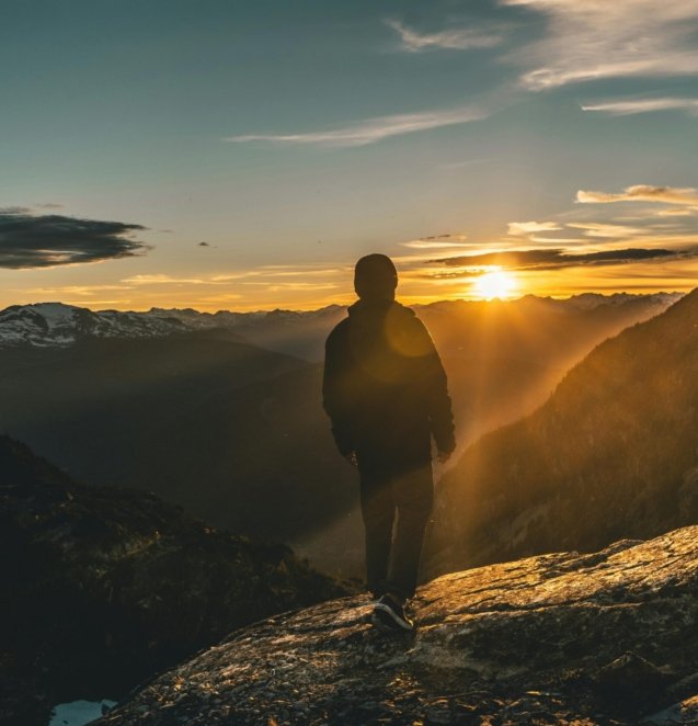 A person standing on a mountain peak at sunrise