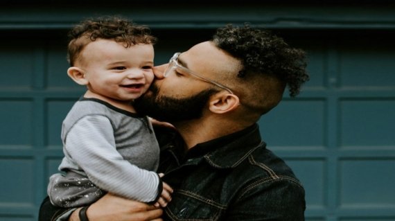 man carrying baby boy and kissing on cheek