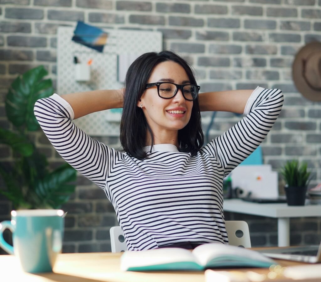 a woman sitting at a desk with her hands behind her head, calm and not overthinking