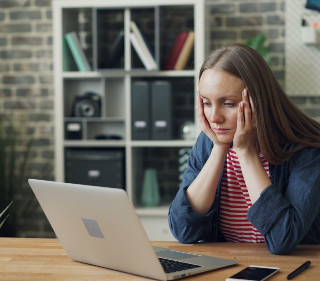 a woman sitting at a table with a laptop in front of her, showing procrastination